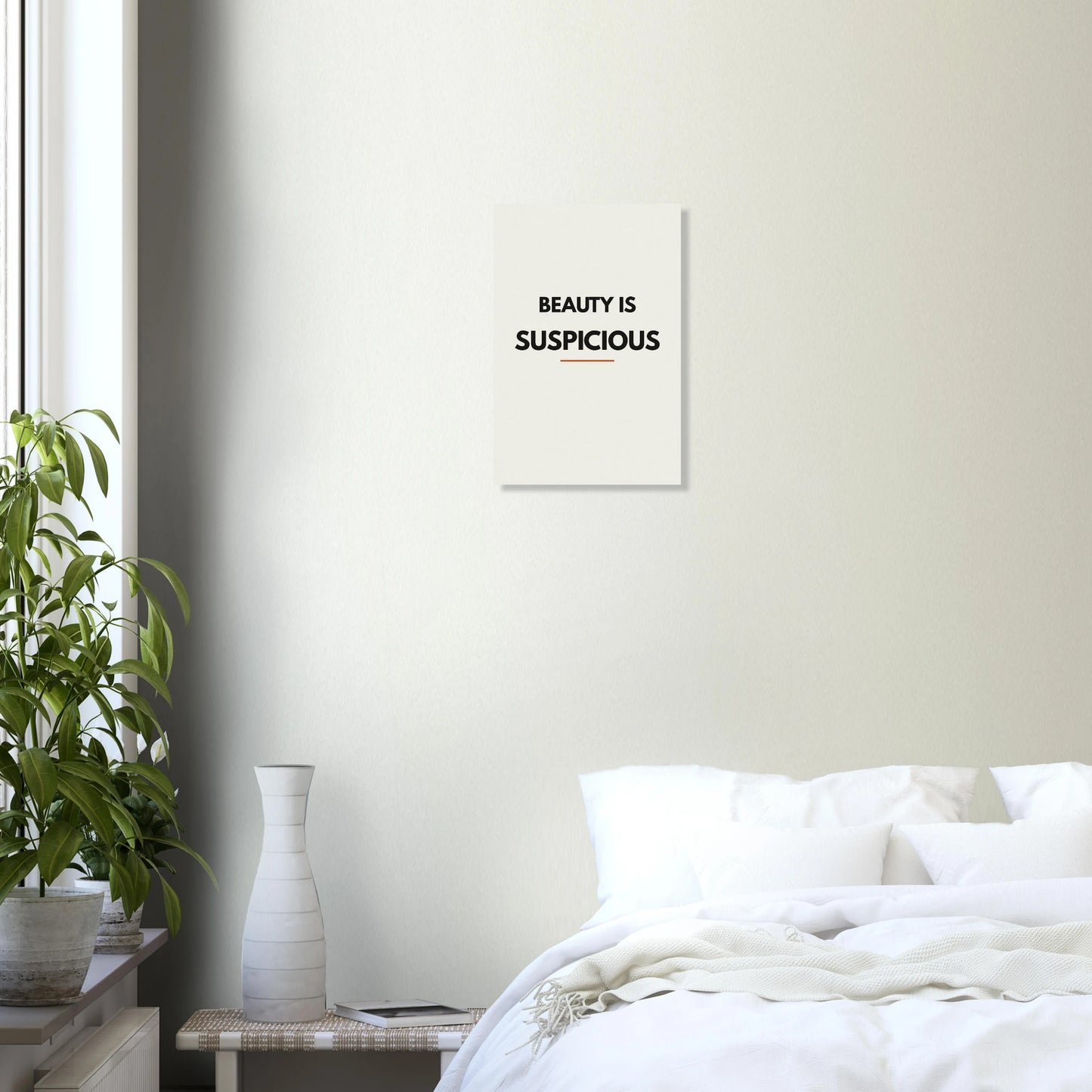 Beauty Is Suspicious typography poster in a bright bedroom with white walls and green plant