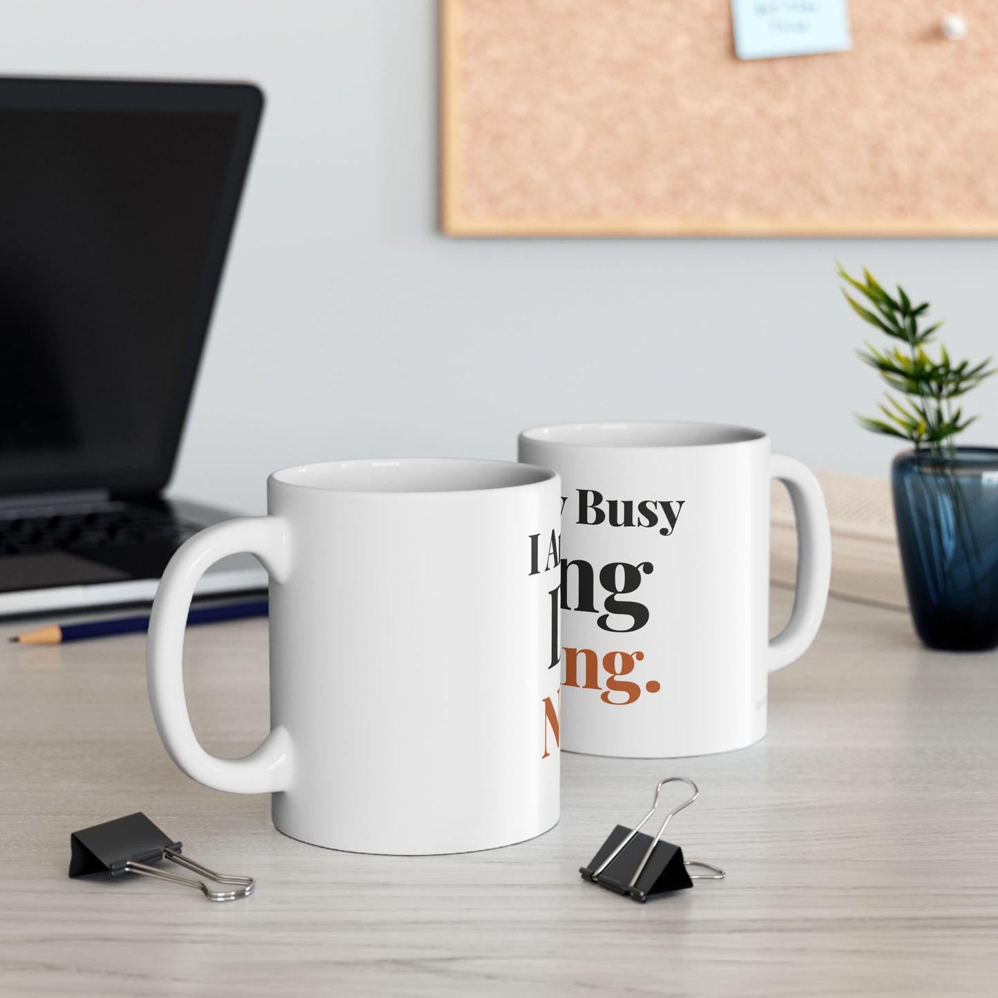 I Am Very Busy Doing Nothing funny typography mugs on a modern office desk with laptop cork board and plant