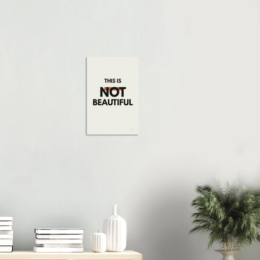 This Is Not Beautiful statement poster in a minimal white room with shelf and plant