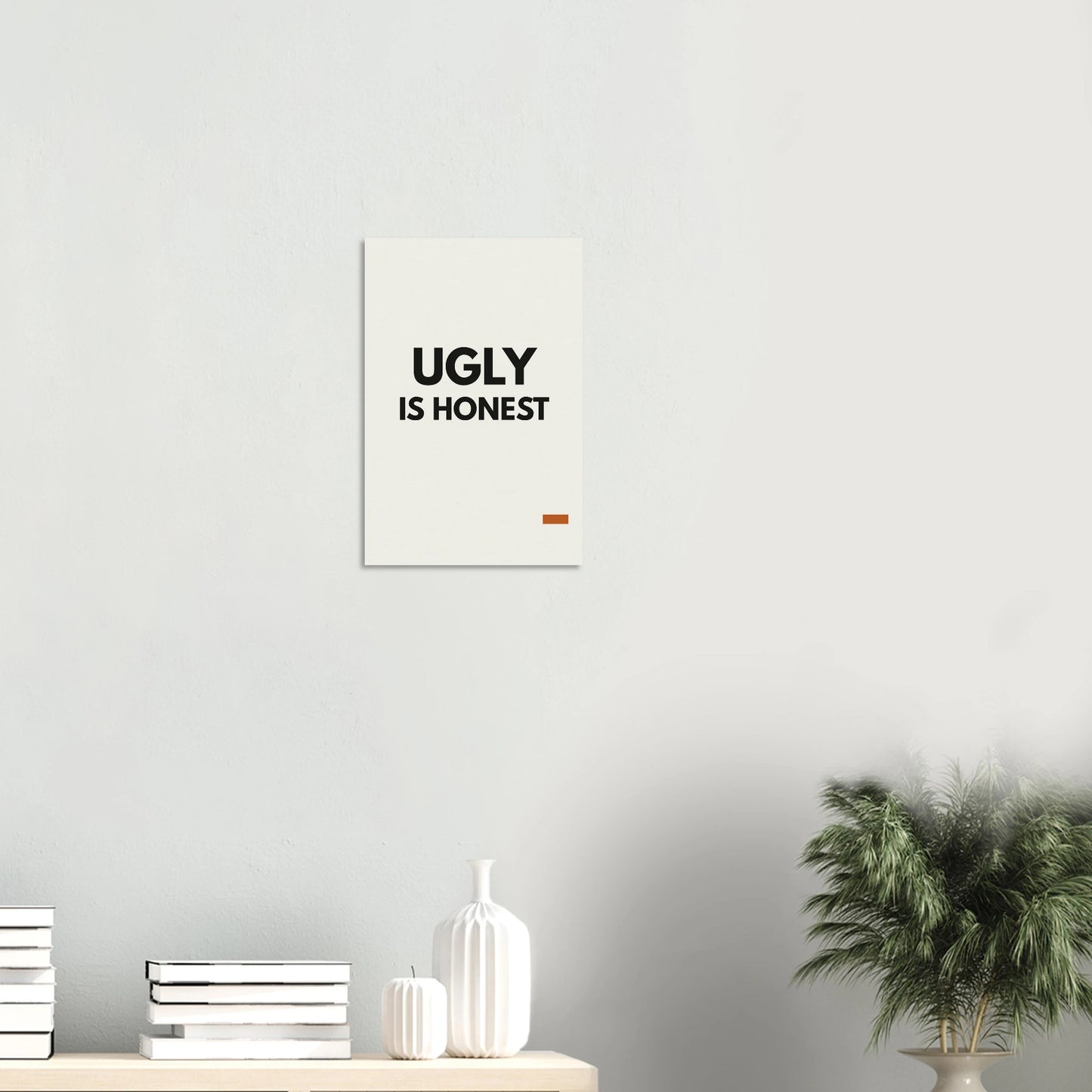 Ugly Is Honest statement poster in a minimal white room with shelf and plant