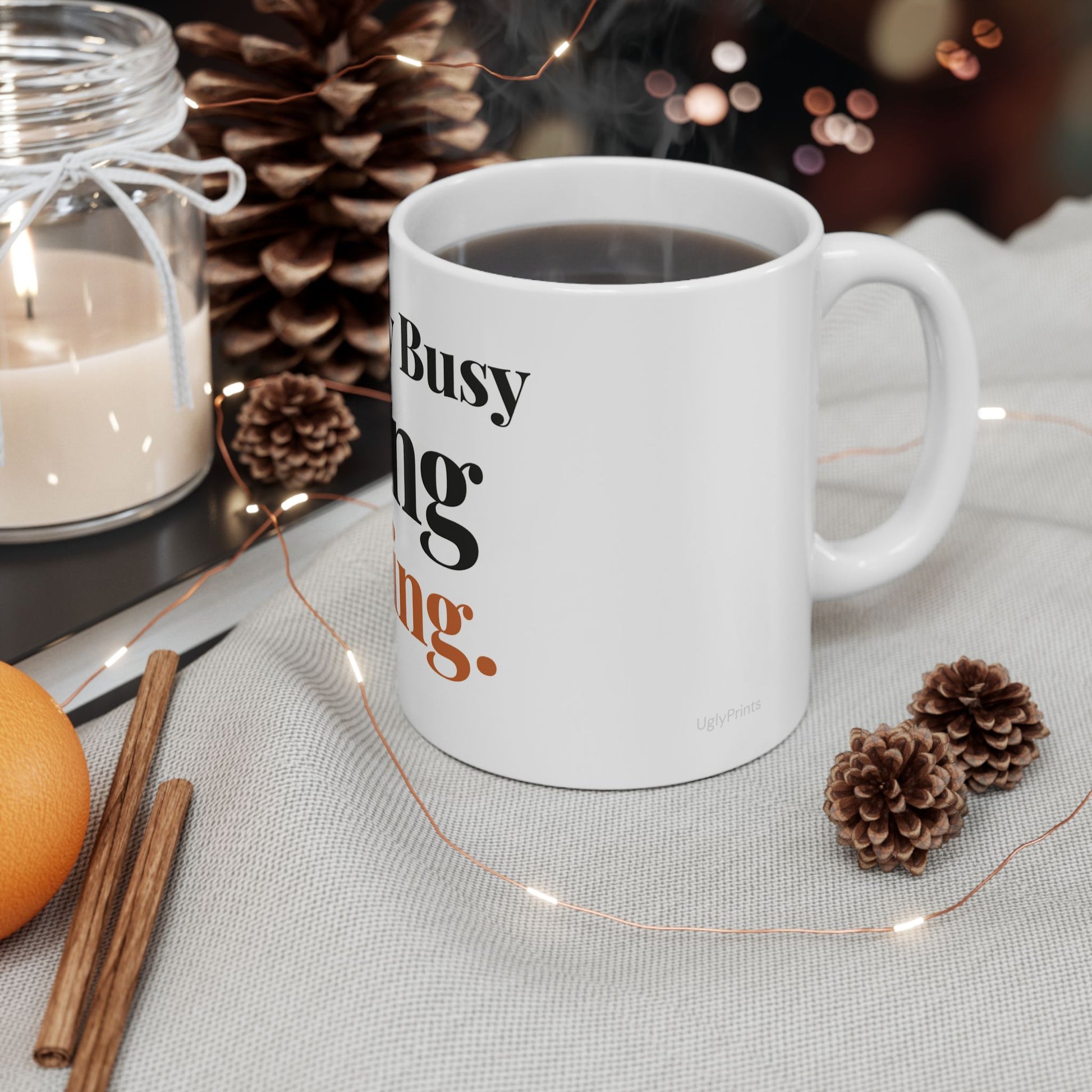 I Am Very Busy Doing Nothing funny office mug styled in a warm cosy setting with pine cones cinnamon and fairy lights