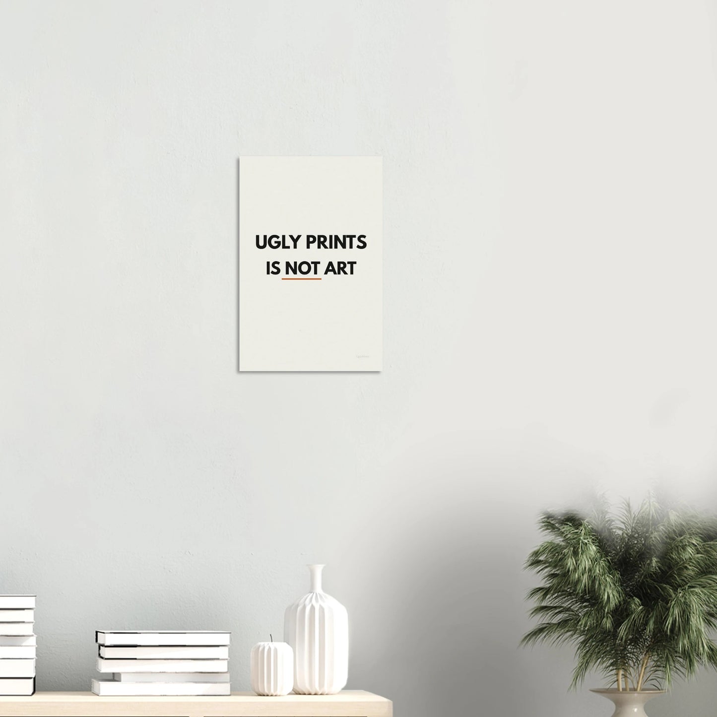 Ugly Prints Is Not Art statement poster in a minimal white room with shelf and plant